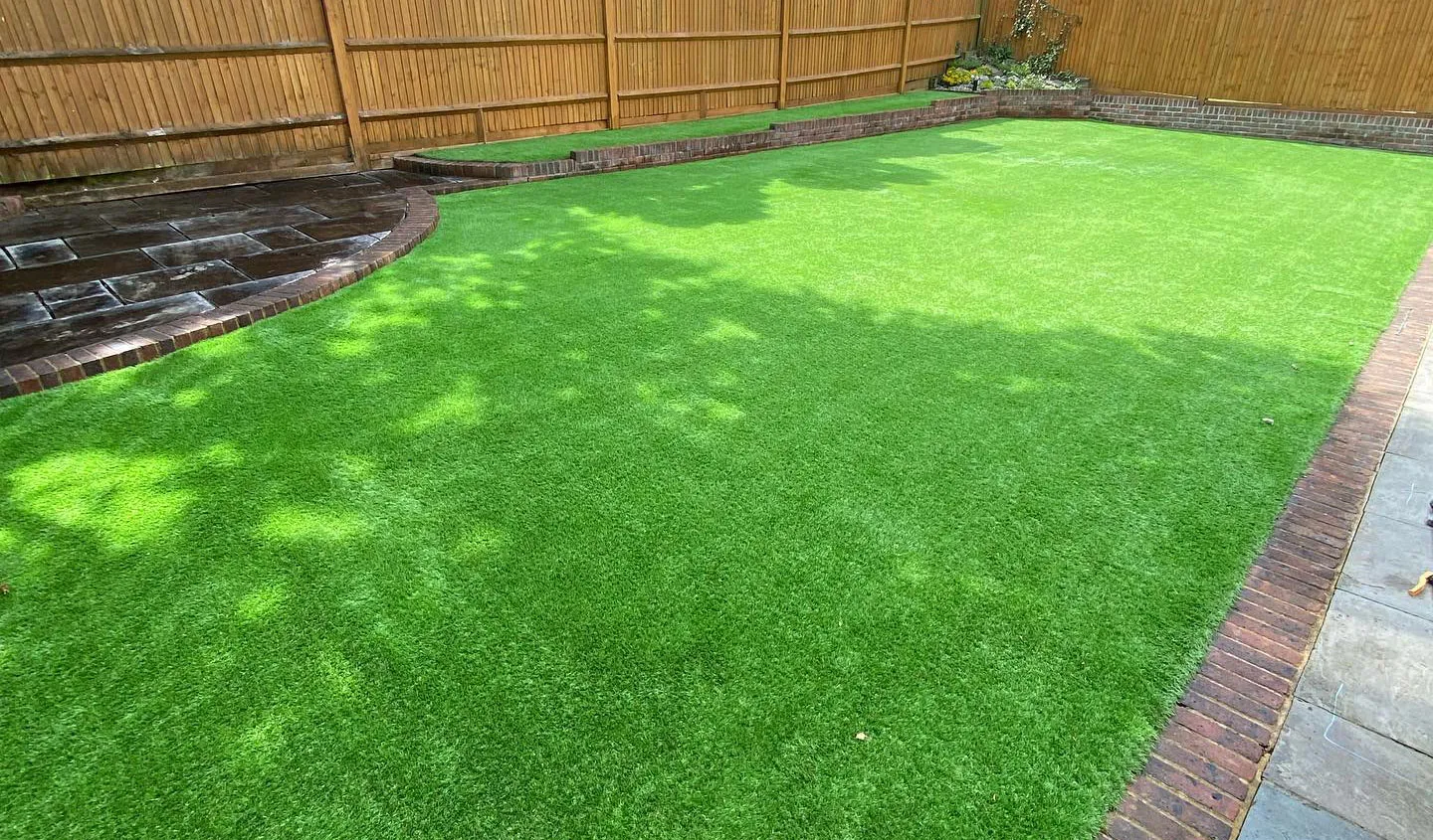 An artificial lawn with brick edging beside a fenced boundary