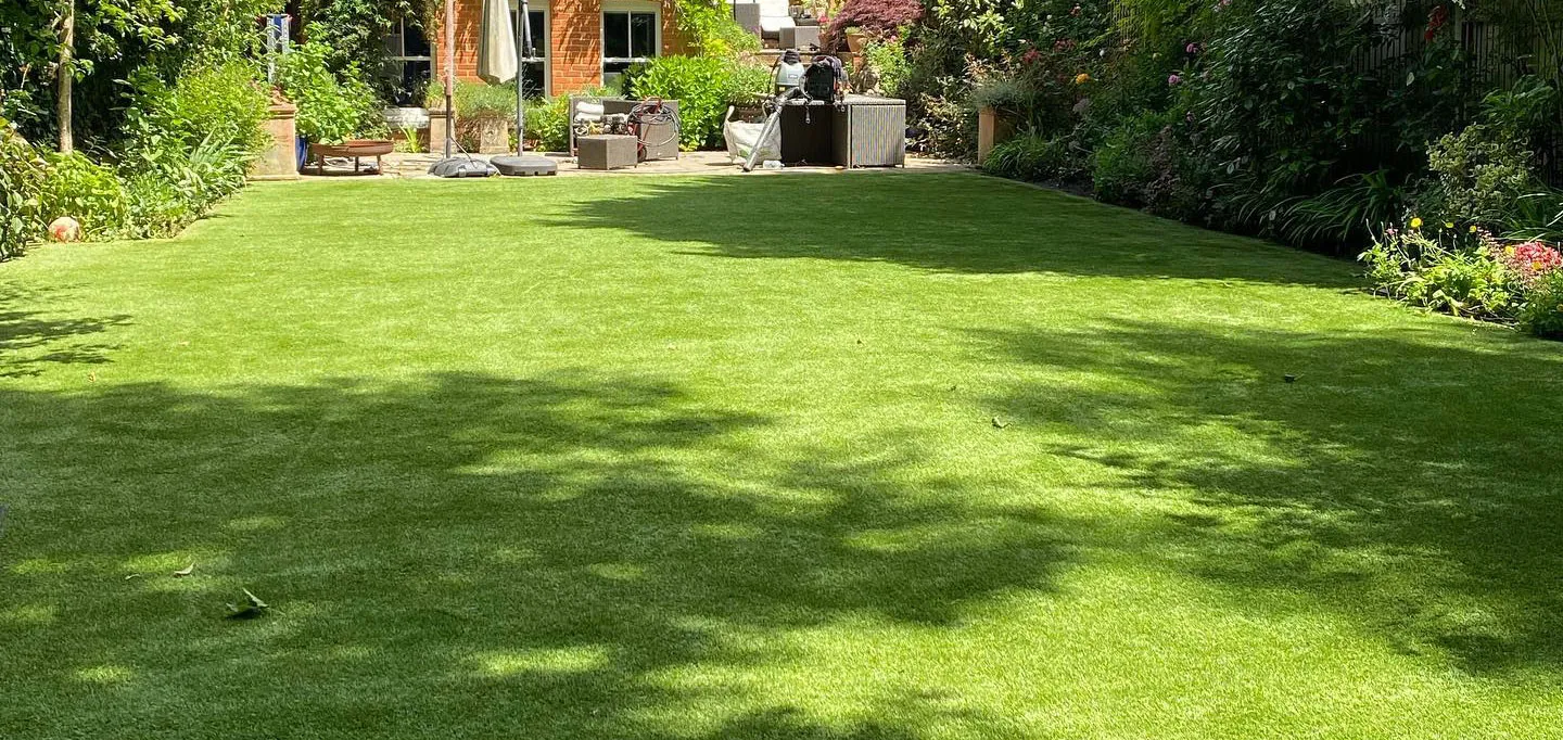 A cleaned artificial lawn with dappled tree shade behind a house